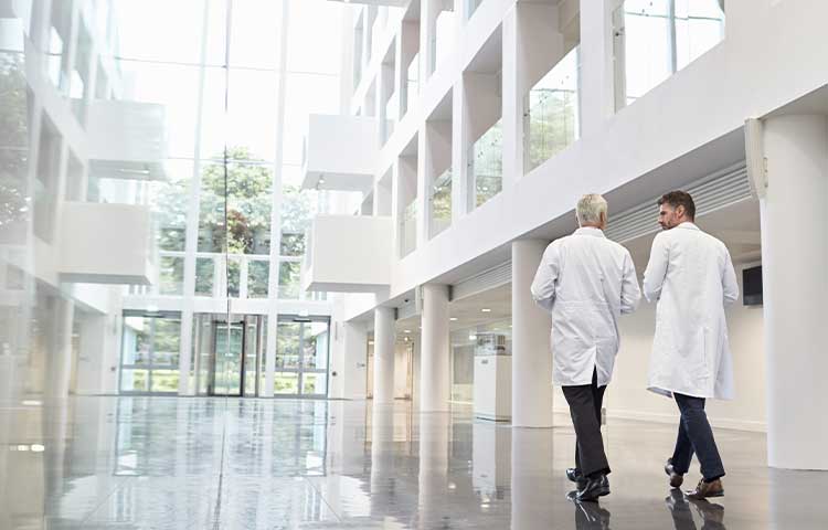 Two men in doctor coats walk down a large hallway