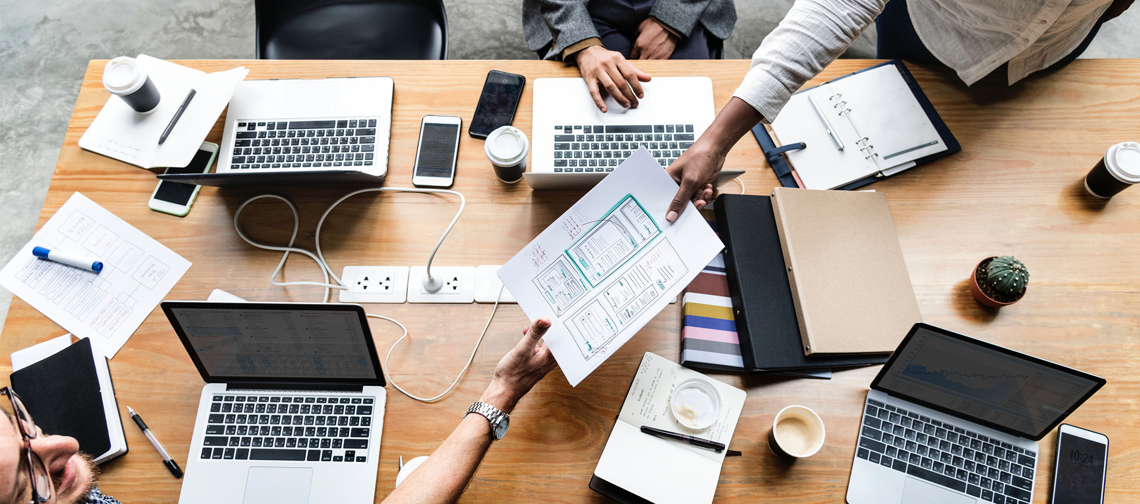3 office workers collaborating at table with laptops sharing paper plans