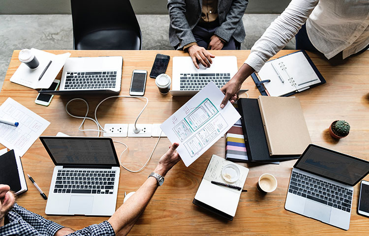 3 office workers collaborating at table with laptops sharing paper plans